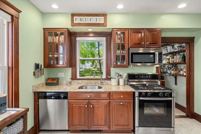 kitchen featuring a sink, glass insert cabinets, light stone countertops, and stainless steel appliances