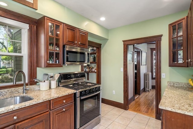 kitchen featuring appliances with stainless steel finishes, a sink, light tile patterned floors, light stone counters, and radiator