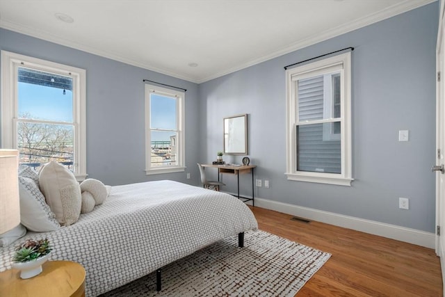bedroom featuring crown molding, baseboards, multiple windows, and wood finished floors