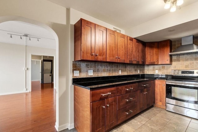 kitchen with backsplash, dark stone counters, wall chimney range hood, light tile patterned floors, and stainless steel stove