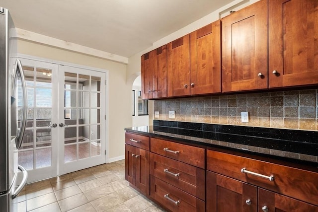 kitchen featuring decorative backsplash, stainless steel fridge, french doors, light tile patterned floors, and dark stone countertops