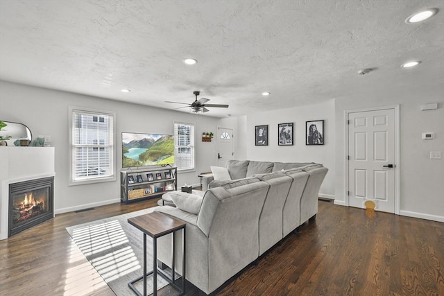 living room featuring dark wood-type flooring, ceiling fan, and a textured ceiling