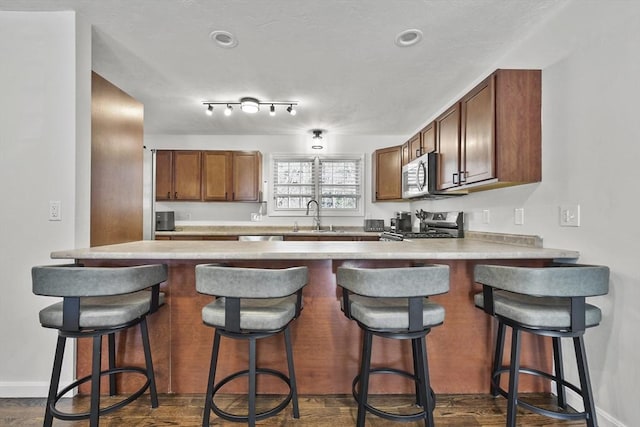 kitchen featuring sink, dark hardwood / wood-style flooring, a kitchen breakfast bar, kitchen peninsula, and stainless steel appliances