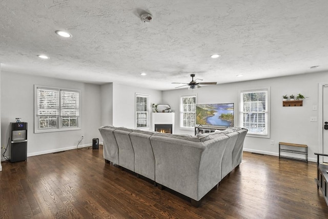 living room featuring ceiling fan, a textured ceiling, and dark hardwood / wood-style flooring