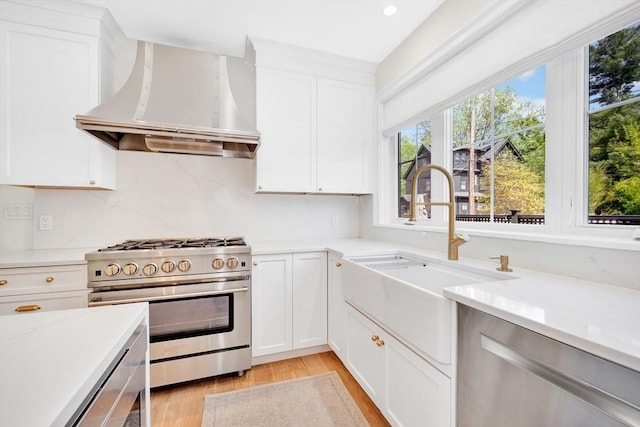7 Newman St, Cambridge, MA 02140 - kitchen featuring appliances with stainless steel finishes, wall chimney range hood, a sink, light wood-style floors, and backsplash