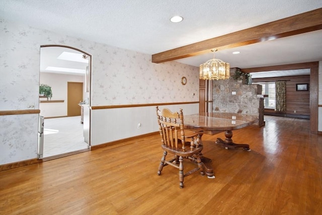 dining area with beam ceiling, a notable chandelier, a textured ceiling, and light wood-type flooring