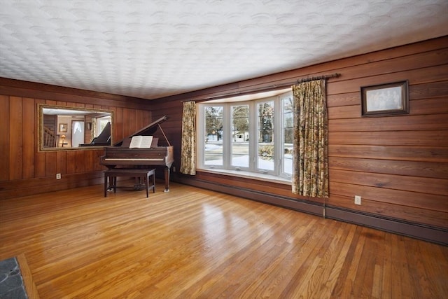 miscellaneous room featuring a baseboard radiator, light hardwood / wood-style floors, and wooden walls