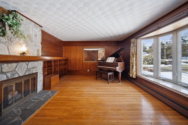 sitting room featuring baseboard heating, wooden walls, a stone fireplace, and hardwood / wood-style floors