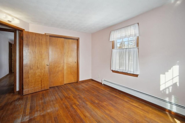 unfurnished bedroom featuring a closet, dark hardwood / wood-style floors, and baseboard heating