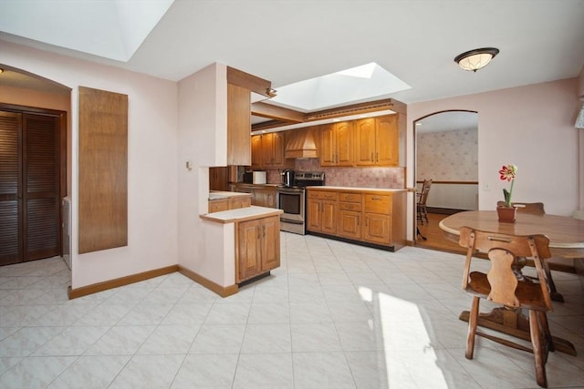 kitchen with electric stove, light tile patterned floors, premium range hood, a skylight, and kitchen peninsula