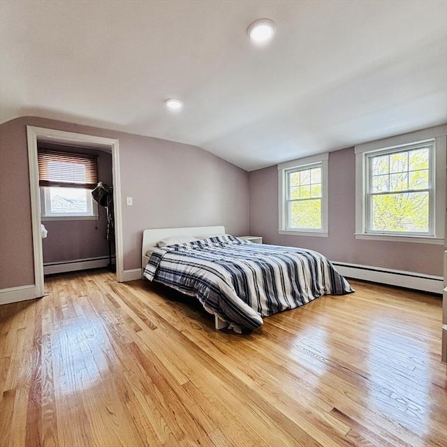 bedroom featuring a baseboard radiator, multiple windows, light wood finished floors, and lofted ceiling