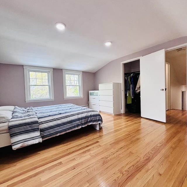 bedroom with light wood-style floors, vaulted ceiling, and a spacious closet
