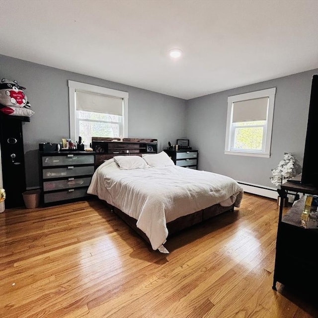 bedroom featuring light wood-type flooring, a baseboard heating unit, and multiple windows