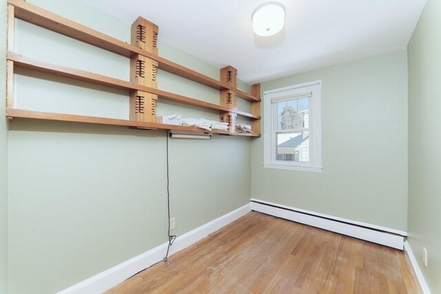 empty room featuring baseboards, a baseboard radiator, and wood finished floors