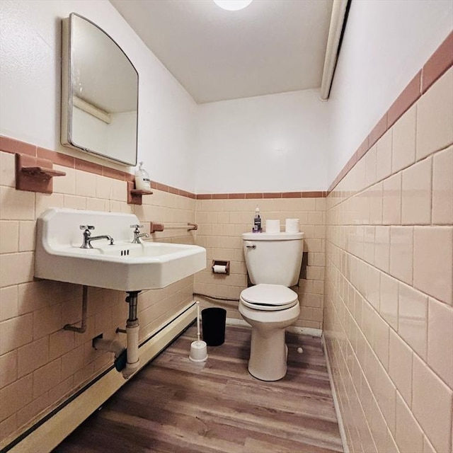 half bath featuring wainscoting, a sink, toilet, tile walls, and wood finished floors