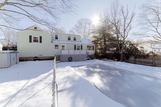 snow covered house with fence, a storage unit, and an outbuilding