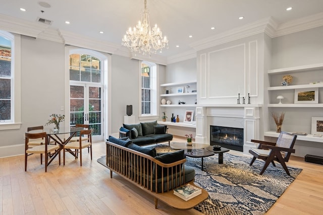 living room featuring built in shelves, french doors, an inviting chandelier, light wood-type flooring, and ornamental molding