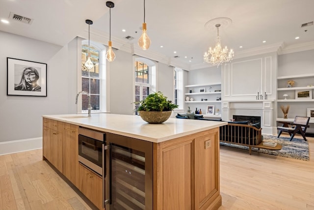 kitchen with light wood-type flooring, an island with sink, wine cooler, and sink