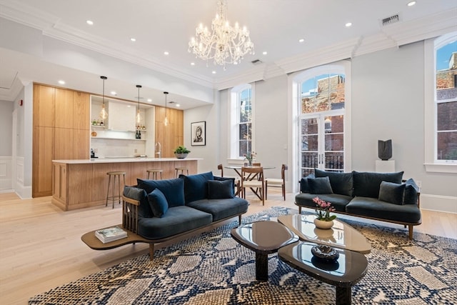 living room featuring a healthy amount of sunlight, light hardwood / wood-style floors, ornamental molding, and a chandelier