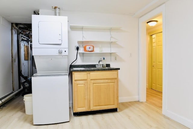 clothes washing area with sink, light wood-type flooring, and stacked washer / dryer