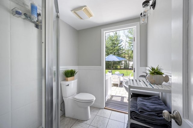 full bath with tile patterned floors, a shower with door, wainscoting, and toilet