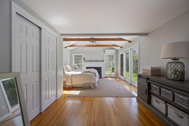 bedroom with lofted ceiling with beams, access to exterior, a fireplace with flush hearth, a wall unit AC, and wood finished floors