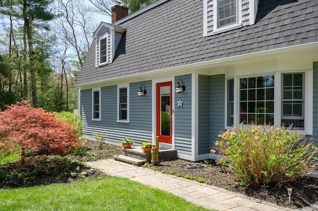 entrance to property with a lawn, a chimney, and roof with shingles