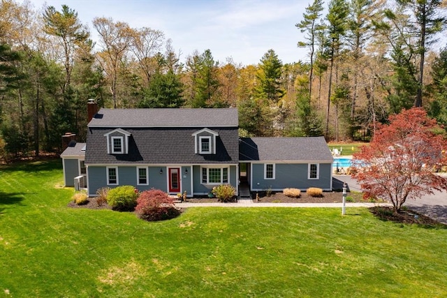 colonial inspired home featuring a forest view, a chimney, a shingled roof, and a front lawn