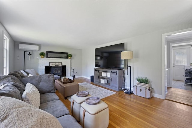 living area with baseboards, a fireplace, light wood finished floors, and a wall mounted air conditioner