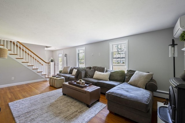 living area featuring a wall mounted AC, baseboard heating, wood finished floors, stairway, and baseboards