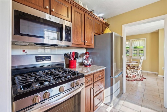 45 Washington St Unit B7, Methuen, MA 01844 - kitchen with stainless steel appliances, brown cabinetry, light tile patterned flooring, backsplash, and baseboards
