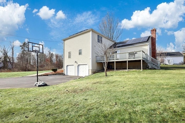 back of property featuring solar panels, a yard, a garage, and a wooden deck