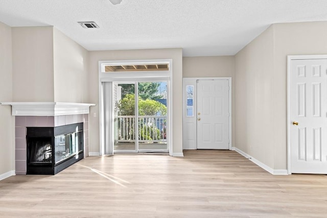 foyer entrance featuring a fireplace, a textured ceiling, baseboards, wood finished floors, and visible vents
