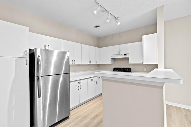 kitchen featuring rail lighting, light countertops, freestanding refrigerator, light wood finished floors, and under cabinet range hood