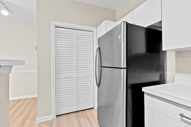 kitchen featuring light countertops, a textured ceiling, freestanding refrigerator, white cabinetry, and light wood-type flooring