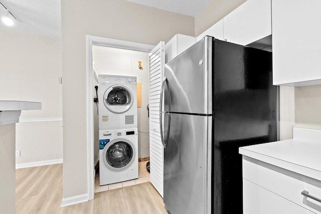 washroom featuring laundry area, baseboards, stacked washing maching and dryer, a textured ceiling, and light wood-style flooring