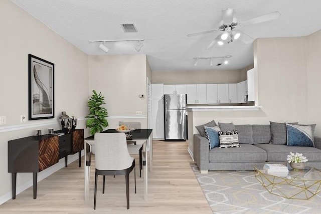 living room with rail lighting, a ceiling fan, light wood finished floors, and visible vents