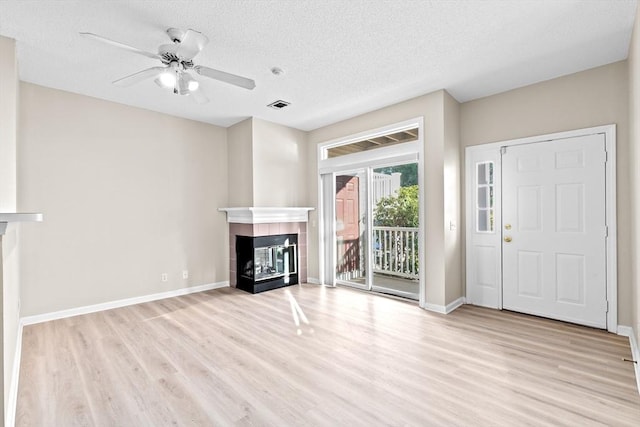 unfurnished living room featuring a tiled fireplace, baseboards, wood finished floors, and visible vents