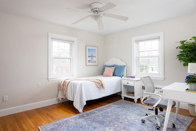 bedroom featuring a ceiling fan, baseboards, multiple windows, and hardwood / wood-style floors