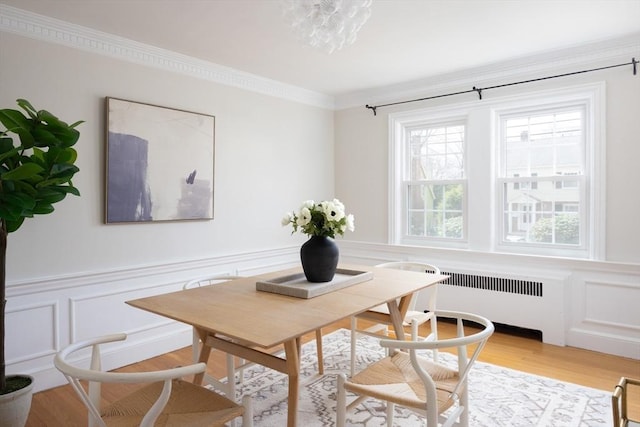 dining space with crown molding, wainscoting, light wood-style floors, a decorative wall, and radiator heating unit