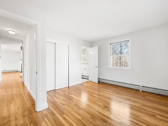 unfurnished bedroom with light wood-type flooring, baseboard heating, and a closet