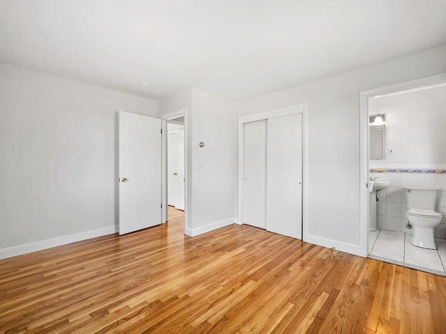 unfurnished bedroom featuring connected bathroom, light hardwood / wood-style floors, a closet, and tile walls