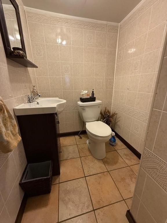 bathroom with toilet, tile walls, ornamental molding, vanity, and tile patterned flooring