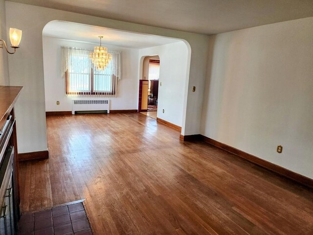 55 Kilburn St, Revere, MA 02151 - unfurnished dining area with arched walkways, radiator heating unit, dark wood-style flooring, baseboards, and a notable chandelier