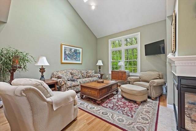 living room featuring a glass covered fireplace, high vaulted ceiling, and light wood-type flooring