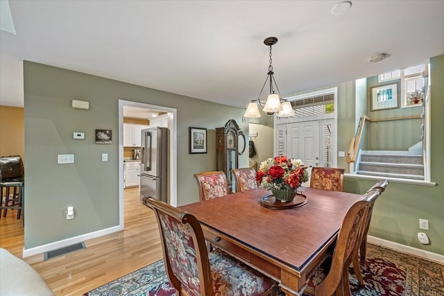dining area with light wood finished floors, baseboards, stairs, and a chandelier