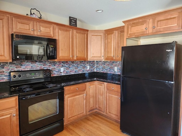 kitchen featuring backsplash, light hardwood / wood-style flooring, black appliances, and dark stone counters