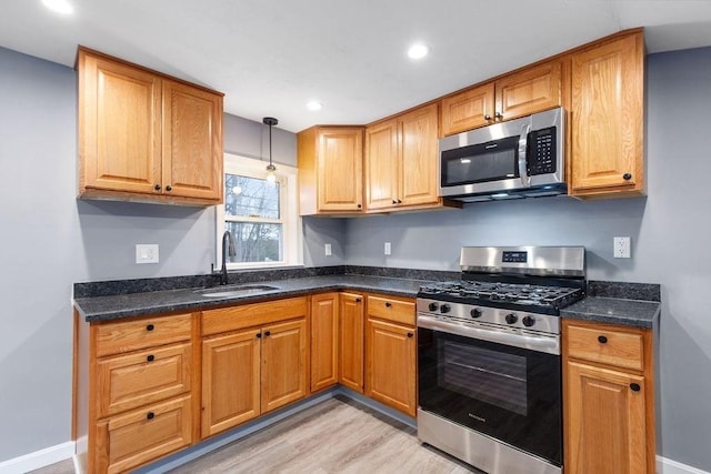 kitchen with sink, decorative light fixtures, light hardwood / wood-style flooring, dark stone countertops, and appliances with stainless steel finishes