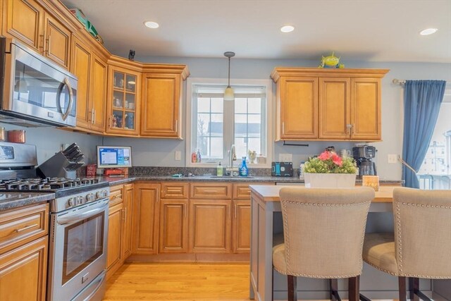 kitchen with a kitchen breakfast bar, appliances with stainless steel finishes, light wood-style floors, brown cabinetry, and a sink