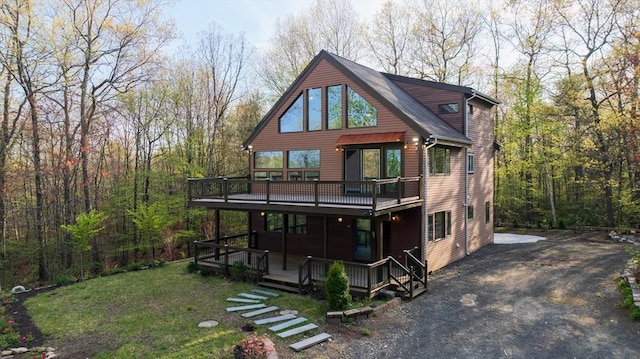 rear view of house with a deck, a forest view, and a lawn